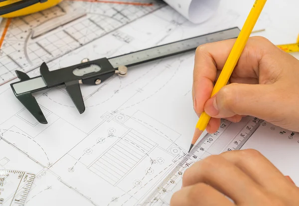 Une personne dessine sur un plan avec un crayon, illustrant le concept de "Maison sur mesure".