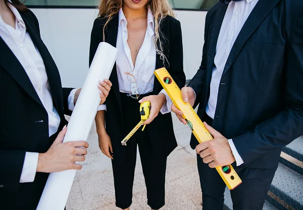 Trois professionnels en costume tenant des outils de construction, représentant 'Maison sur mesure'.