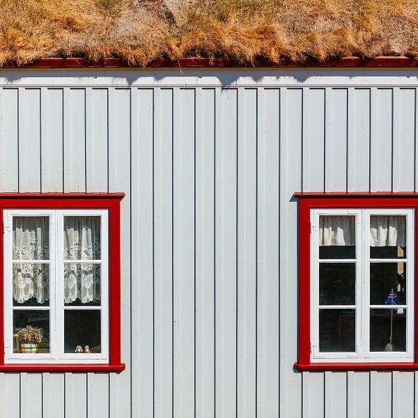 Maison blanche avec des garnitures rouges et deux fenêtres, montrant le revêtement extérieur de la maison.