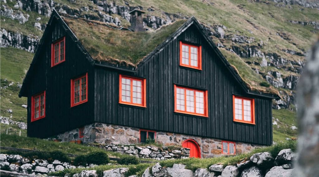 Maison scandinave traditionnelle en bois noir avec des fenêtres rouges et un toit en herbe.